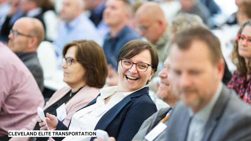 Business professionals smiling and networking during a conference session, representing productivity supported by stress-free, luxury transportation.