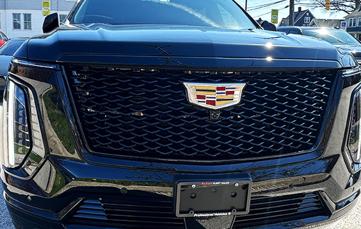 Close-up of the front end of a dark Cadillac SUV, showing the distinctive grille and emblem centered above the license plate area.