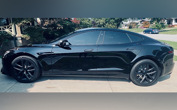 Black luxury coupe parked in a driveway, showing its sleek side profile and large black wheels.
