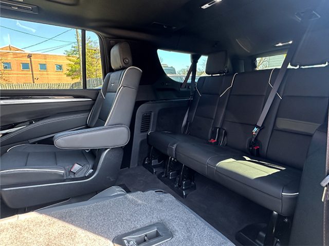 Interior of a vehicle showing two front captain's chairs and a three-seat rear bench with seat belts, daylight visible through windows.