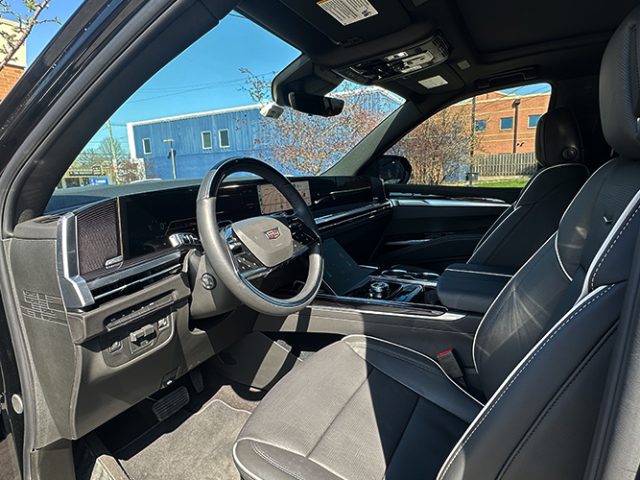 Interior view of a black Cadillac with leather seats, steering wheel, and center console visible from the passenger side door open