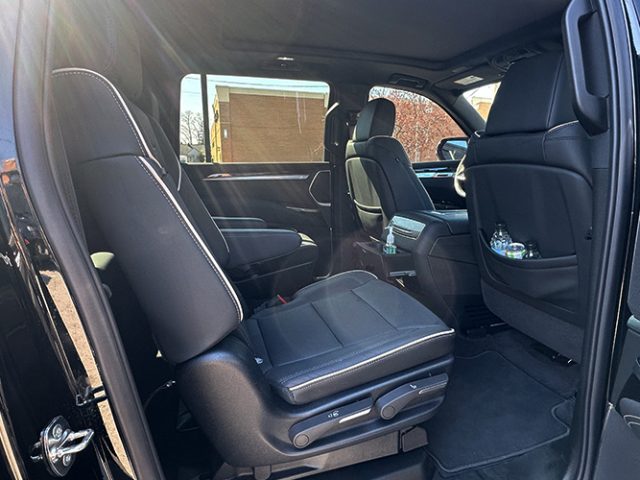 Black leather SUV interior with two captain chairs in the second row, front seat visible, sunlight streaming in through the windows.