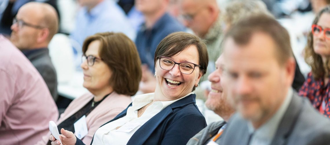 Business professionals smiling and networking during a conference session, representing productivity supported by stress-free, luxury transportation.